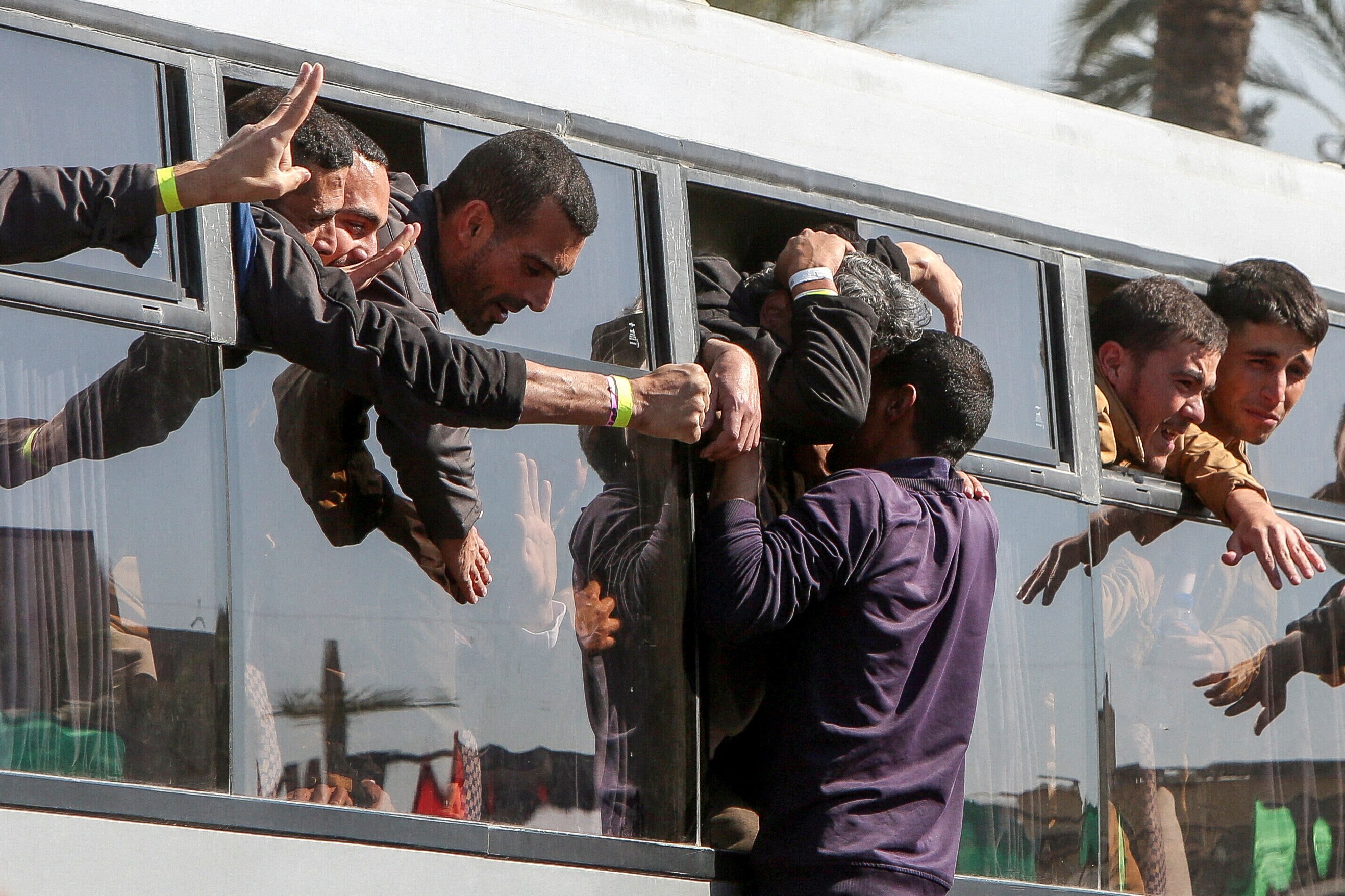 Men stick their heads out of the windows of a bus as others climb up to hug them