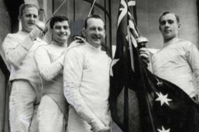 Four Australian male fencers stand with the national flag.