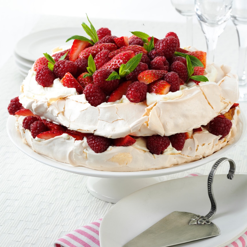 A pavlova with strawberries, mint and whipped cream on top.