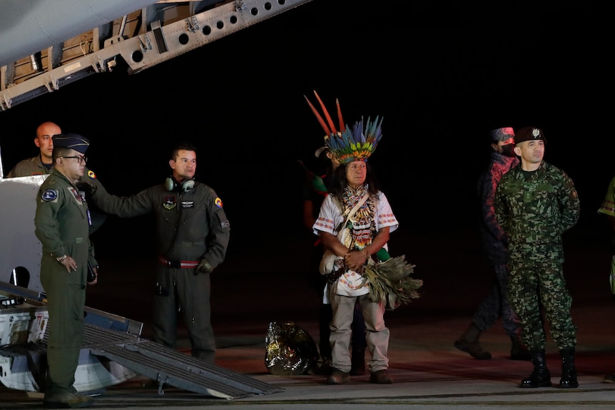Military personnel and Indigenous leaders stand under a plane in Bogota as children found in the jungle are stretchered off
