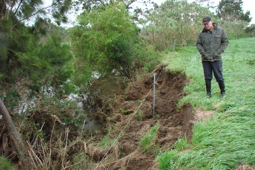 Man in gumboots looks over the erosion damage to his river after the floods Albion Park, New South Wales