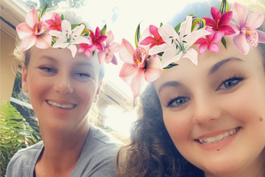 A middle-aged woman smiles next to a younger woman. A photo filter makes it look like there are flowers in their hair.