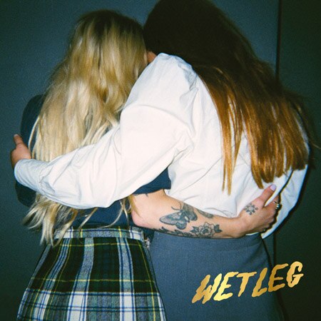 The backs of the two members of Wet Leg, who stand arm in arm