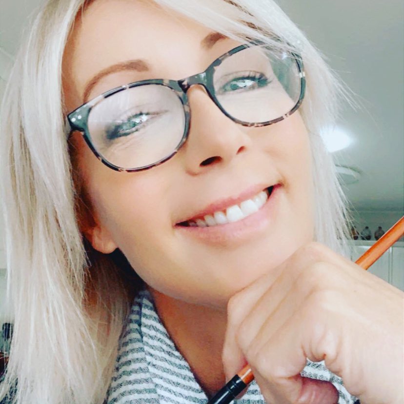 Jen McGregor wears black reading glasses and holds a pencil, smiling.