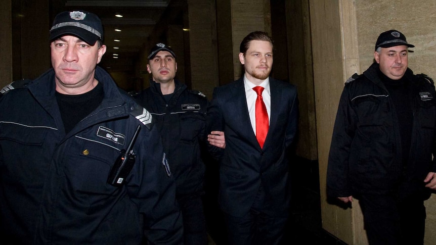 A man in a suit is led by several police officers through a darkened tunnel