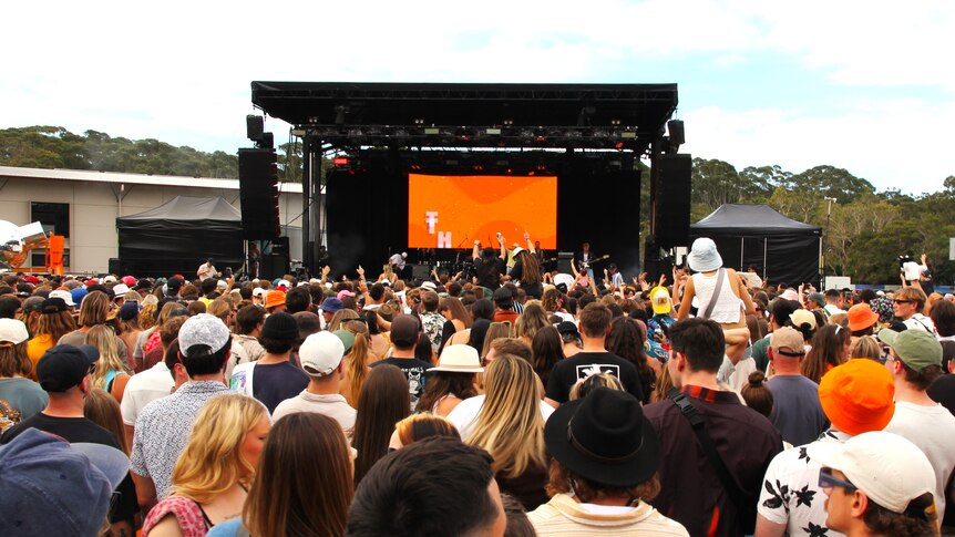 Hundreds of people face the festival mainstage with orange set.