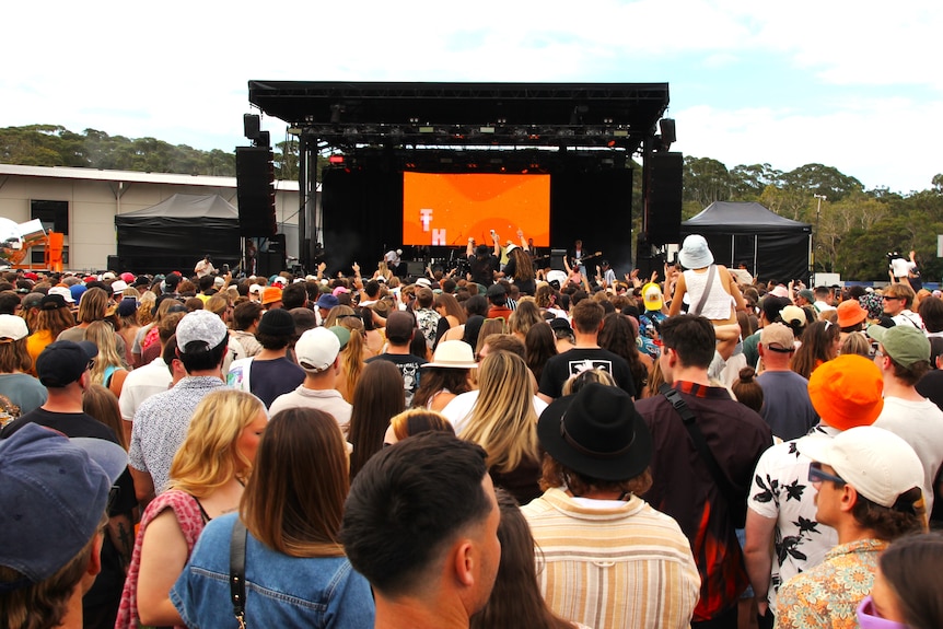 Hundreds of people face the festival mainstage with orange set
