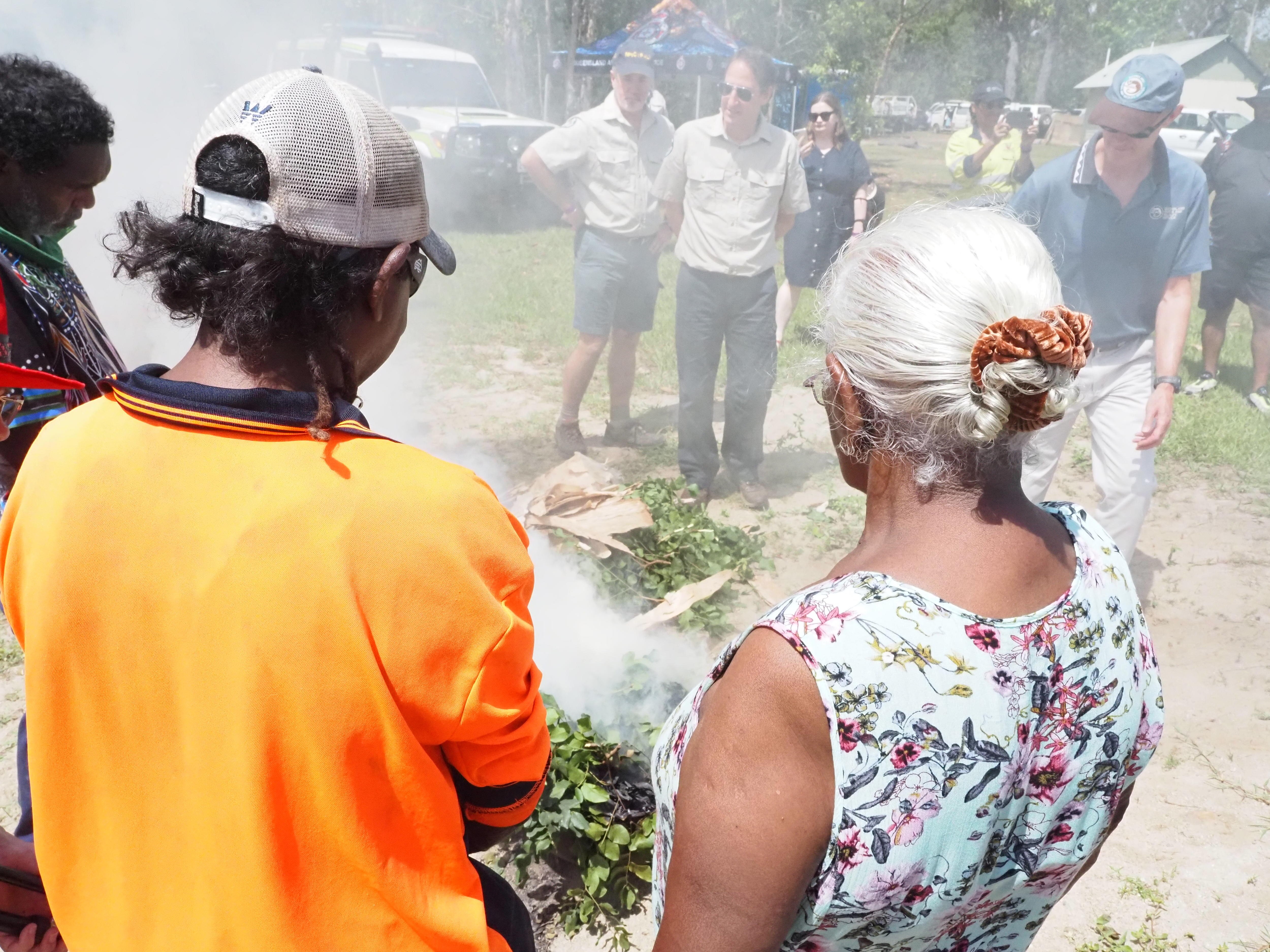 Indigenous people wearing bright clothes perform a smoking ceremony.