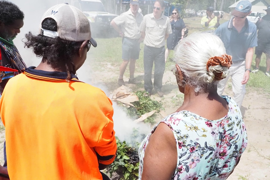 Indigenous people wearing bright clothes perform a smoking ceremony.