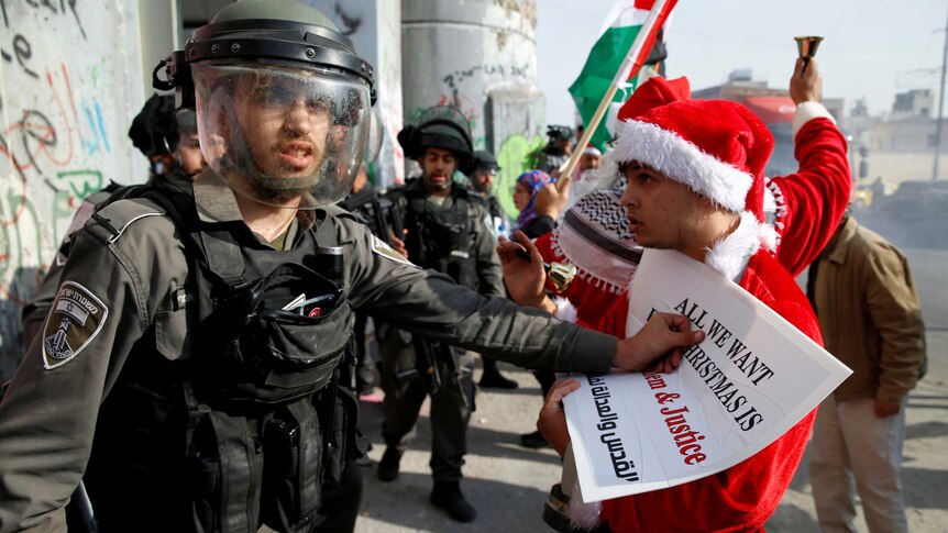 A Israeli border guard and a Palestinian man dressed as Santa argue.