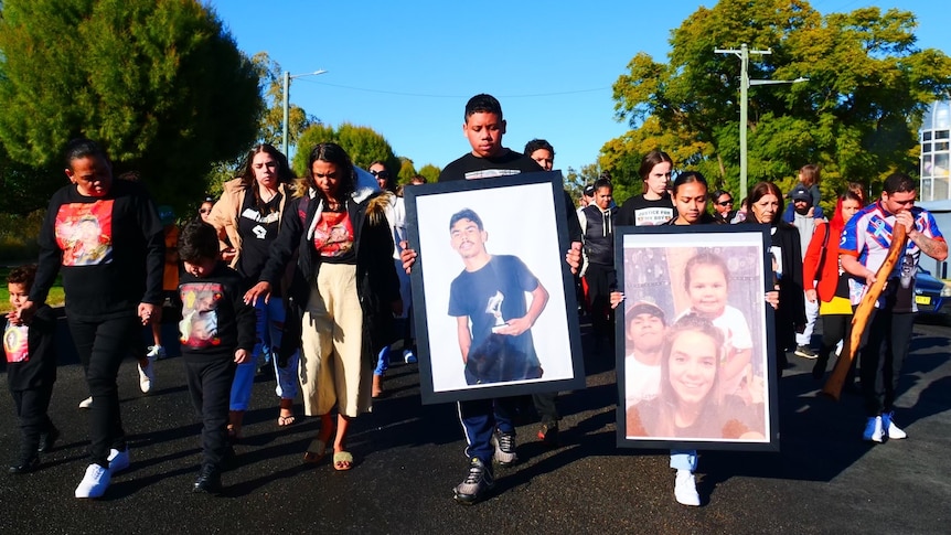 people walking down street with framed pictures of Aboriginal man and his family members.