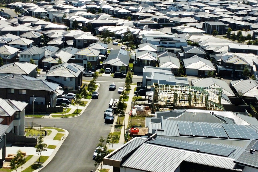 A bird's eye view of dozens of homes in a suburb, with a frame of one house being constructed.