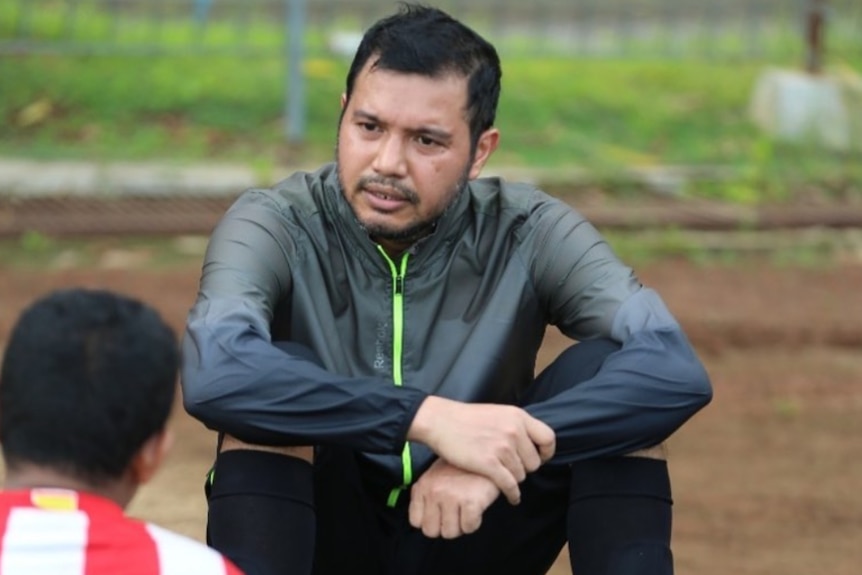 Seorang pria duduk di atas kayu di lapangan sepak bola.