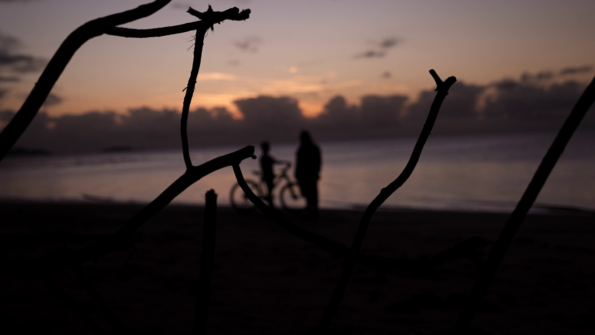 La silueta de un niño en bicicleta y una mujer en la playa al atardecer. 