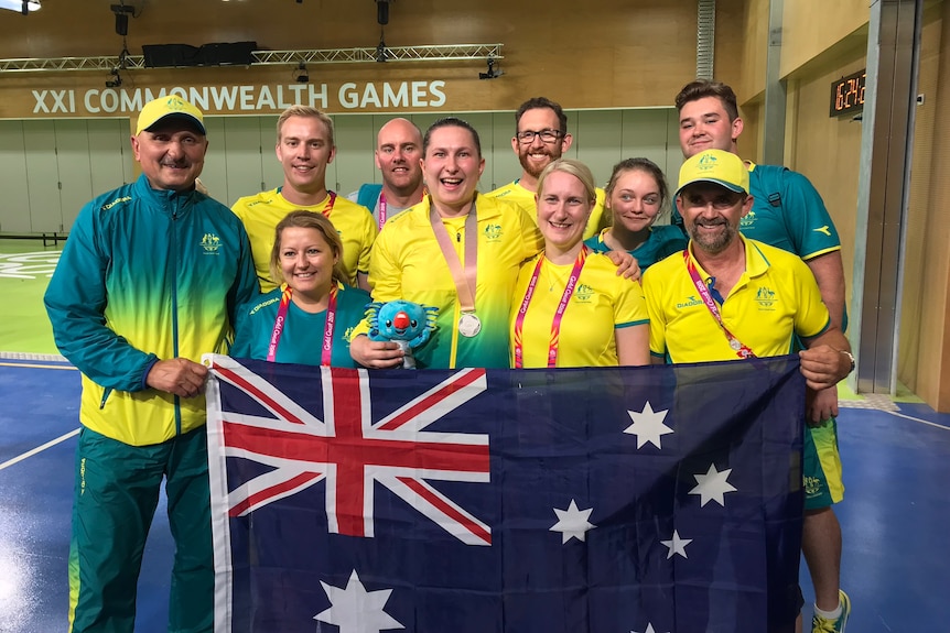 Shooter Elena Galiabovitch wears her silver medal and poses for a photo with her coach and teammates.