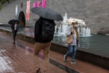 Three people walking past the NGV with umbrellas in the rain.