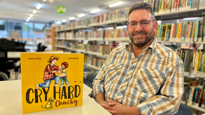 A children's book on a table next to a man looking happy.