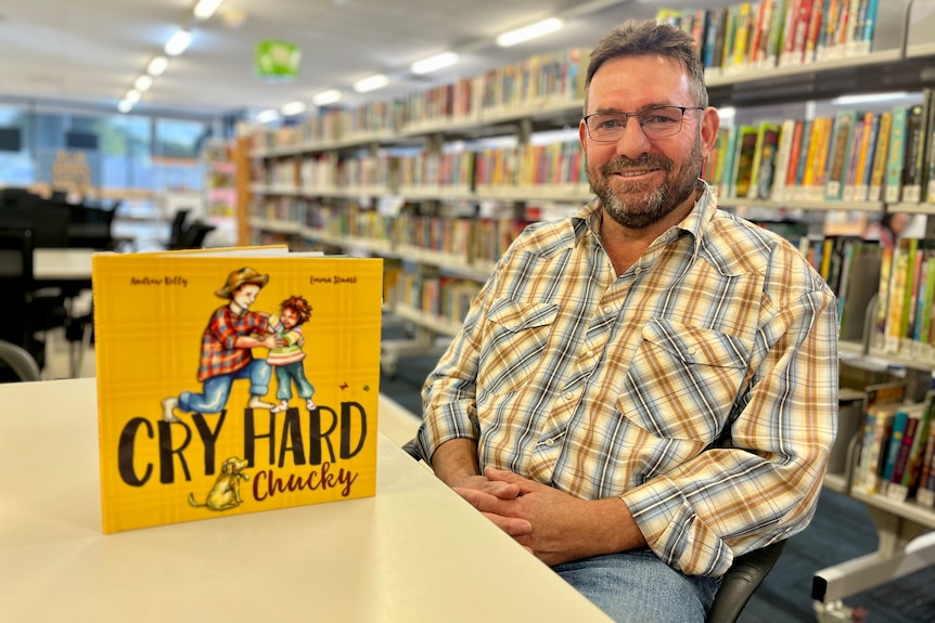A children's book on a table next to a man looking happy.