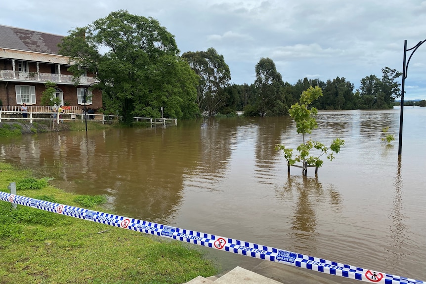 Water creeps up toward an apartment building as people watch from a footpath