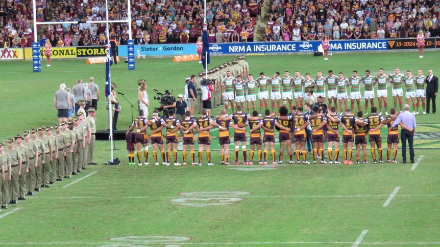 View from the stands of the Broncos and Rabbitohs teams linking arms as they listen to the national anthem being sung.