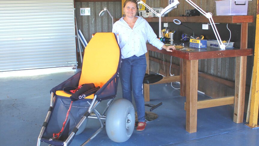 A lady holds a modified wheelchair with large wheels in a workshop