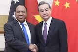 Rimbink Pato shakes hands with Wang Yi in front of PNG and China flags