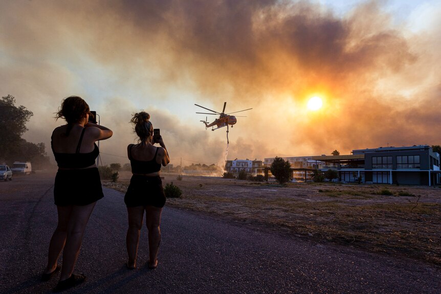Two women young take photos of a helicopter against a smoky sky