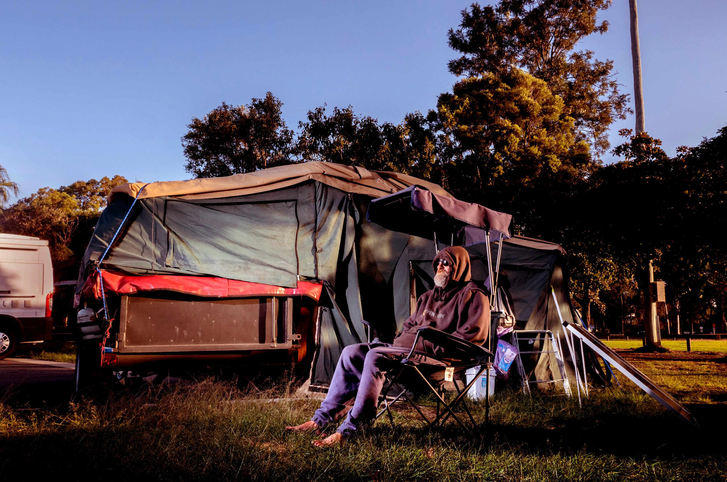 A man with a beard, hoodie and glasses sits outside a tent.