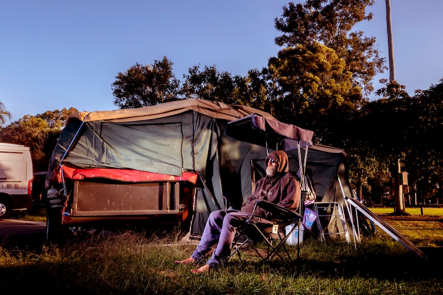 A man with a beard, hoodie and glasses sits outside a tent.