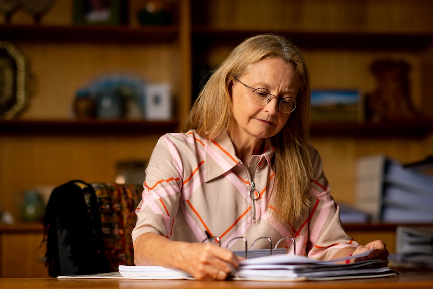 La coroner par intérim du NT, la juge Elisabeth Armitage, assise à un bureau à l'intérieur d'un bureau et écrivant sur des papiers dans un dossier.