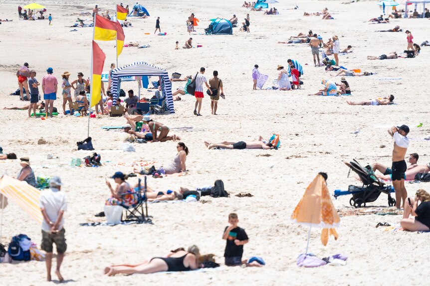 Generic photo of people laying on the sand at a beach in Adelaide on a hot day.
