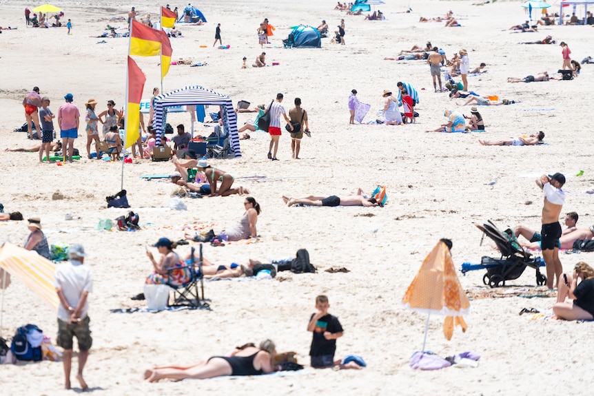 Generic photo of people laying on the sand at a beach in Adelaide on a hot day.