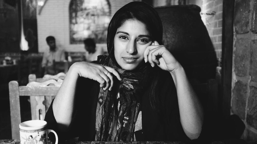 A woman sits down at a table looking directly at the camera.