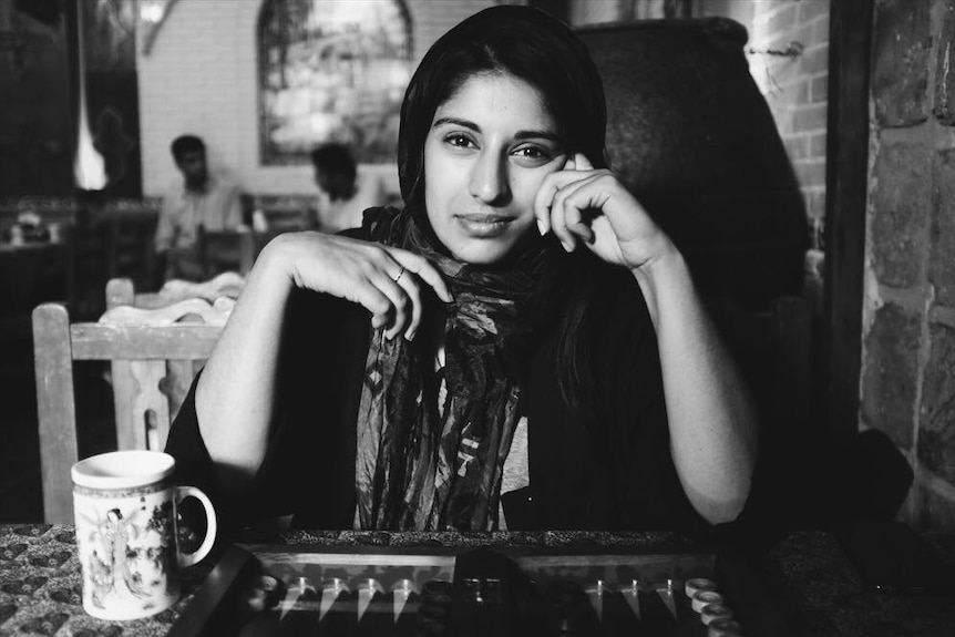 A woman sits down at a table looking directly at the camera.