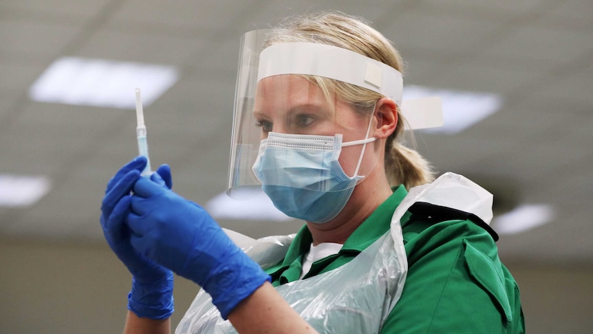 A woman in a face mask and clear shield examines