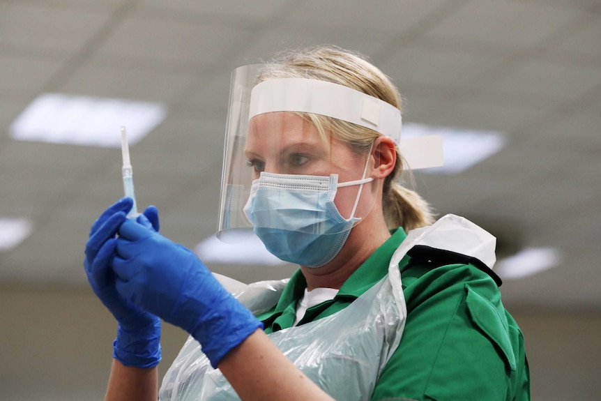 A woman in a face mask and clear shield examines