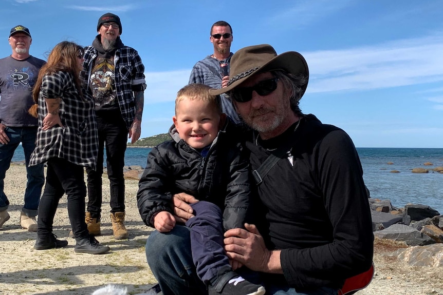 A man kneels with his grandson with four people standing behind.