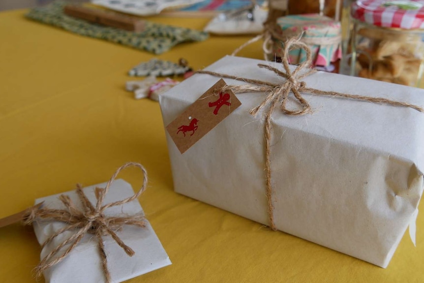 Christmas gifts sit on a table wrapped in brown butchers paper and twine.