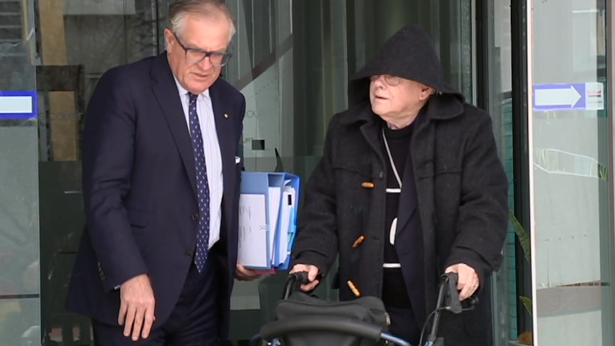 An elderly man in a black hood using a walker.