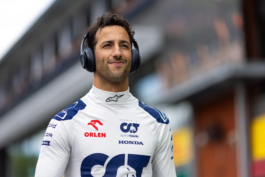 F1 driver Daniel Ricciardo walks through pitlane, in his racing suit, wearing headphones