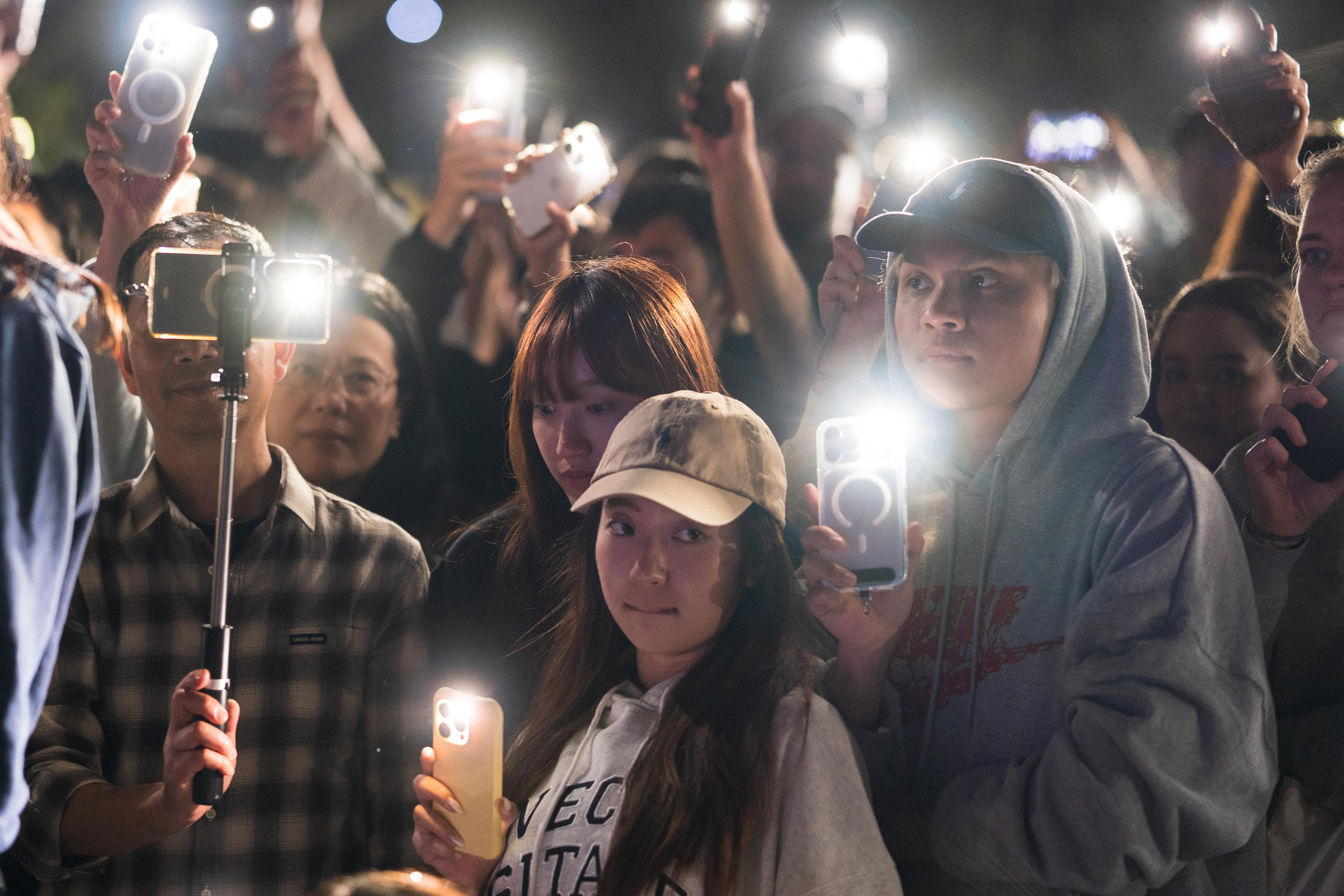 Un grupo de personas sostiene teléfonos con antorchas encendidas y enciende velas por la noche.