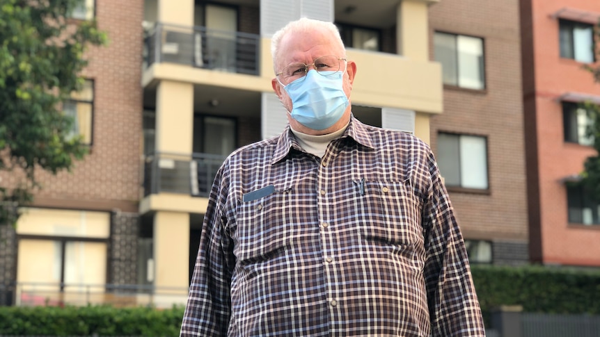 A man wearing a face mask stands outside an apartment development.