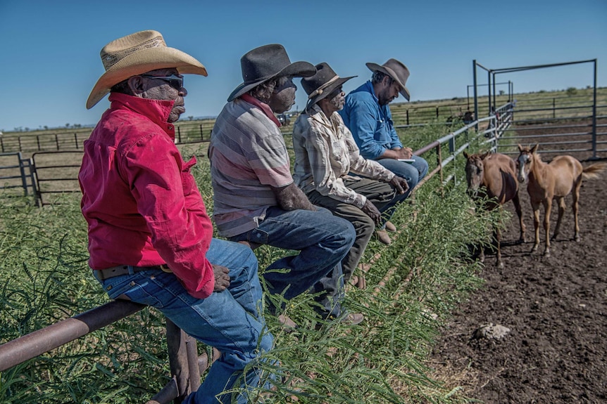 Four indigenous workers at Noonkanbah Station, sitting on a rail