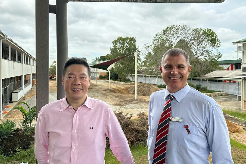 Asian man in pink shirt with Causasian man in blue shirt and tie in front of construction zone