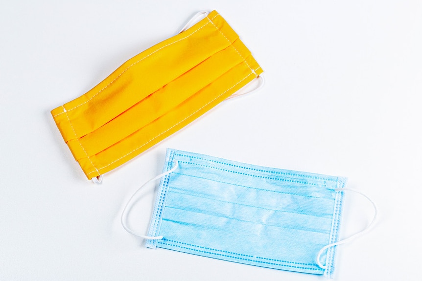 A reusable yellow fabric face mask and a blue single-use surgical face mask.