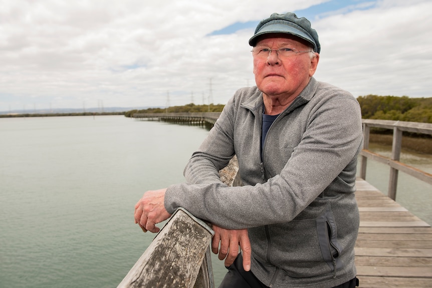 A man wearing a hat looks at the camera from a boardwalk over water