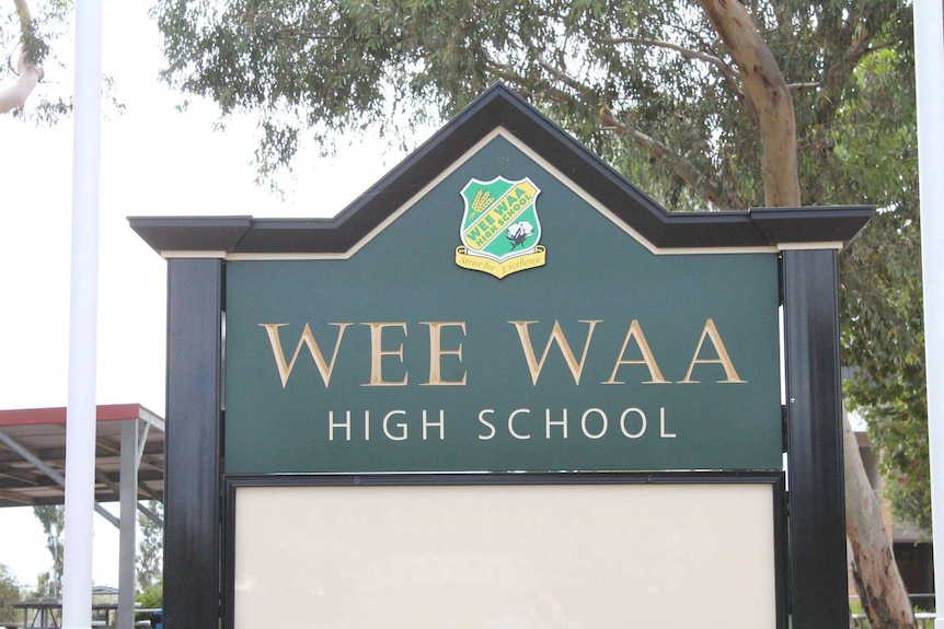 A green sign at the front of Wee Waa High School in north west NSW, with trees and an awning in the background.