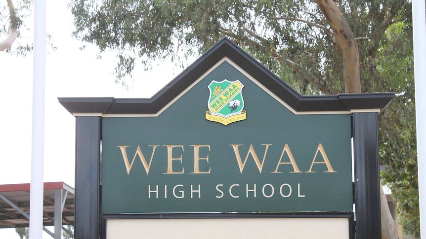 A green sign at the front of Wee Waa High School in north west NSW, with trees and an awning in the background.