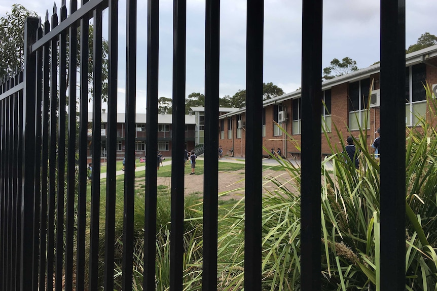 Students standing in the playground at Floraville Public School, as seen through the school's fence.