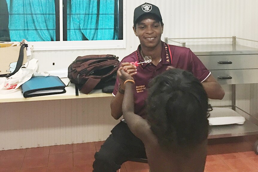 Aboriginal interpreter distracting small child with bubbles.